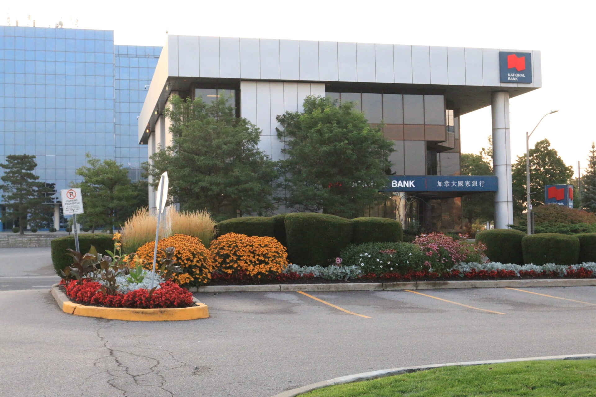 Modern bank building with glass facade and landscaped entrance. Colorful flowers and greenery surround the entrance. Signage features both English and Chinese text.