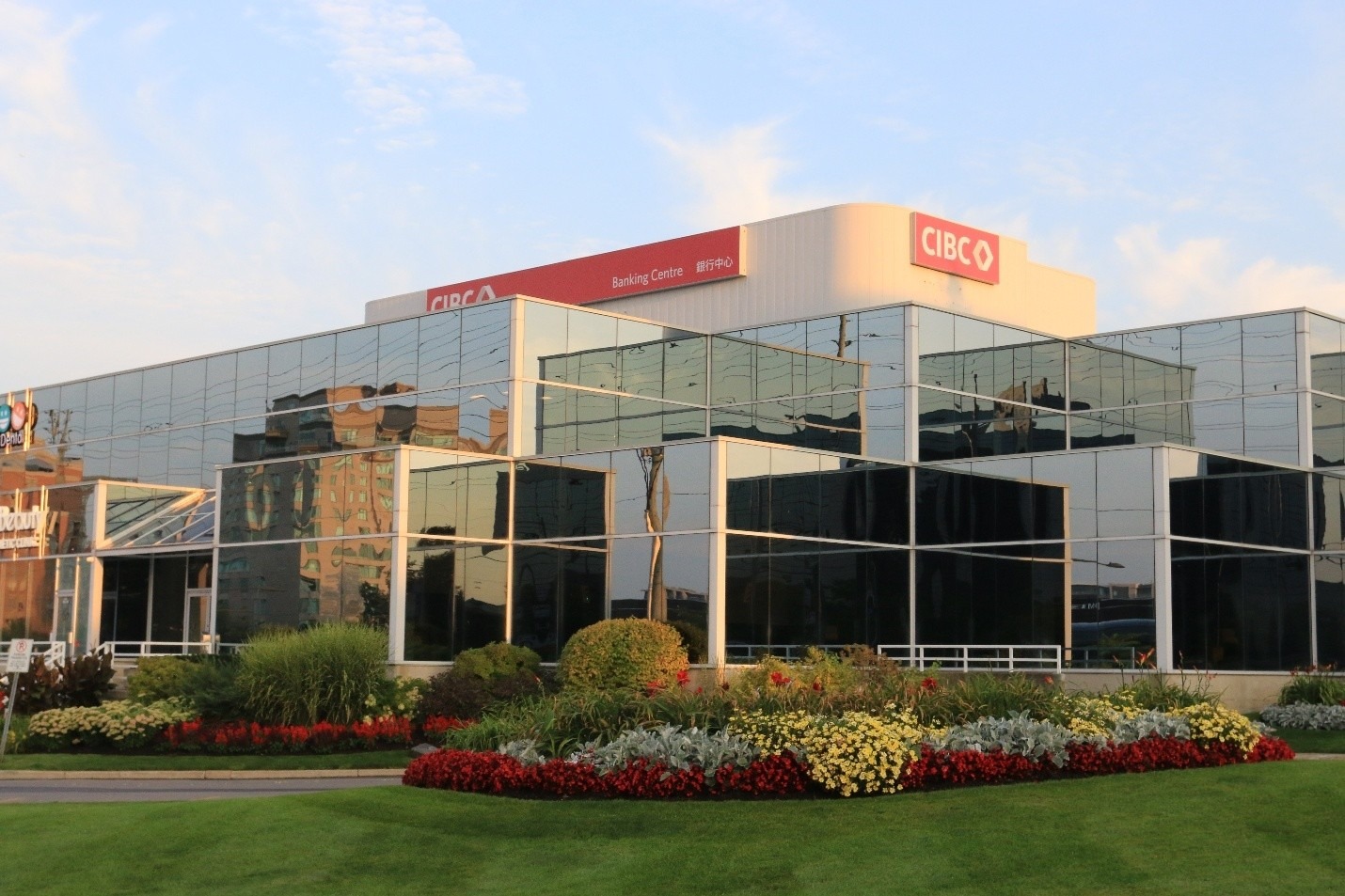 Modern glass building with CIBC signage, surrounded by neatly landscaped gardens and vibrant flowers under a sunny blue sky, creating a professional appearance.