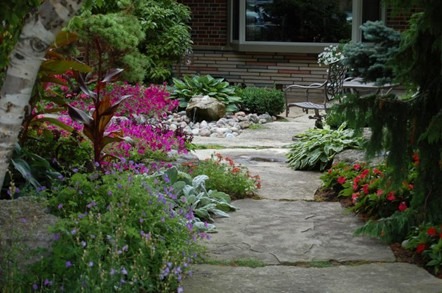 A lush garden path with colorful flowers, shrubs, and a stone walkway leading to a bench. No visible landmarks or historical buildings.