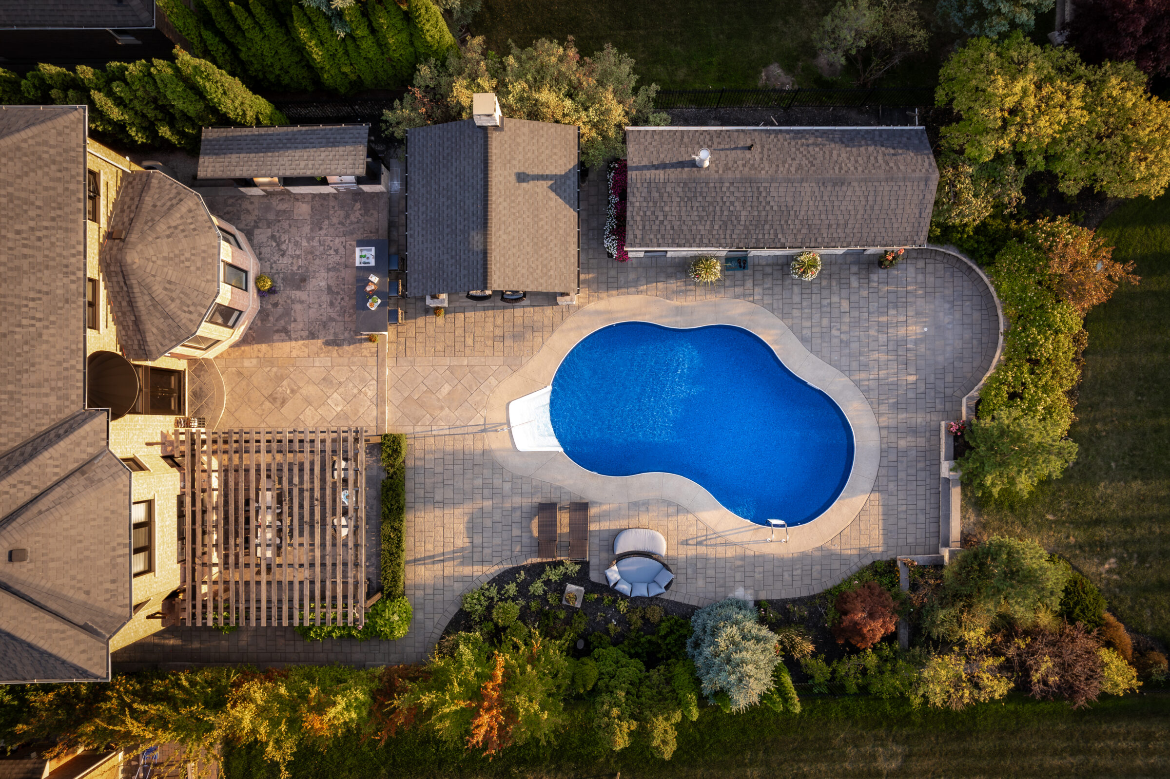 Aerial view of a backyard featuring a kidney-shaped swimming pool, deck chairs, and surrounding greenery, creating a serene and private outdoor oasis.