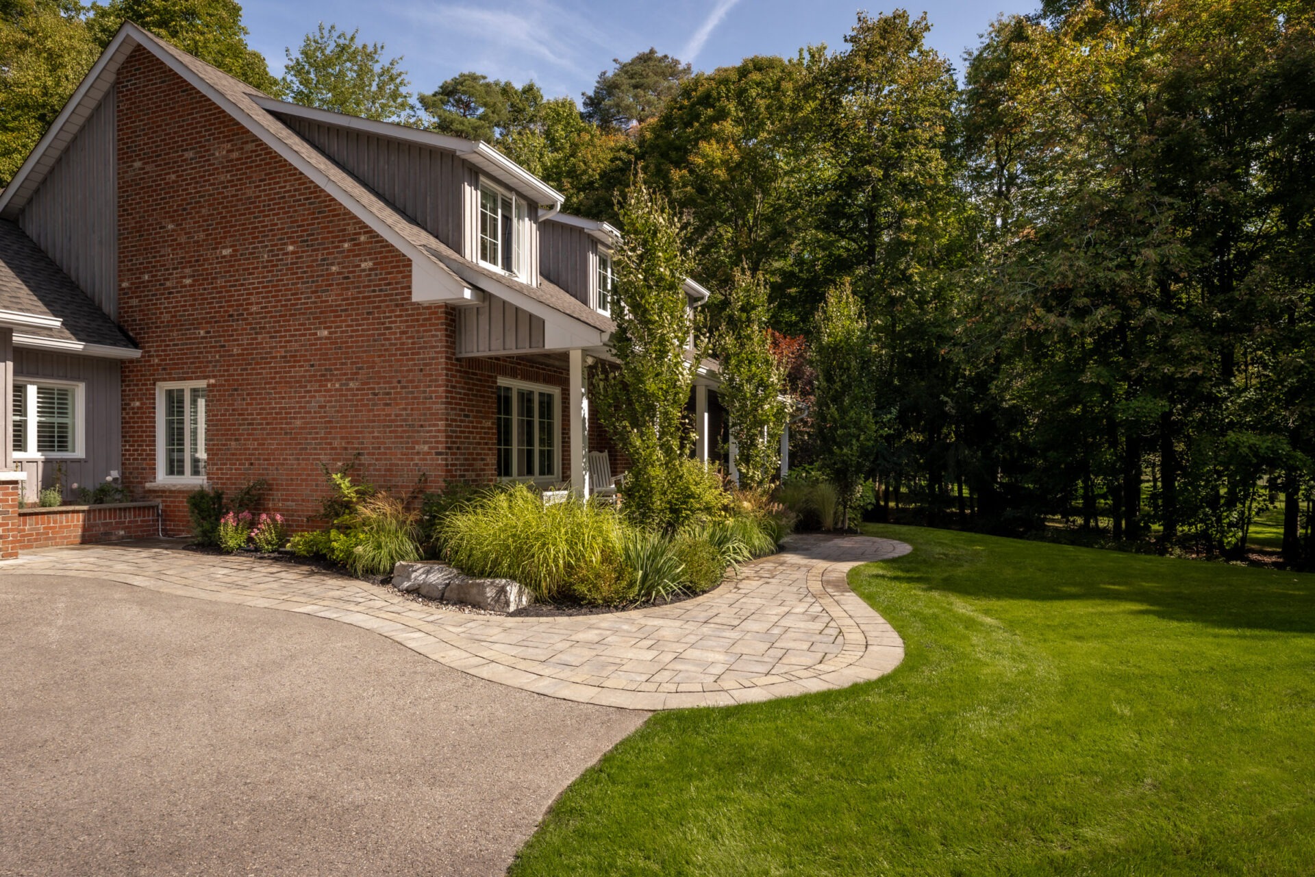 Brick house with manicured lawn and curved stone pathway, surrounded by lush greenery. No visible landmarks or historical buildings are present.