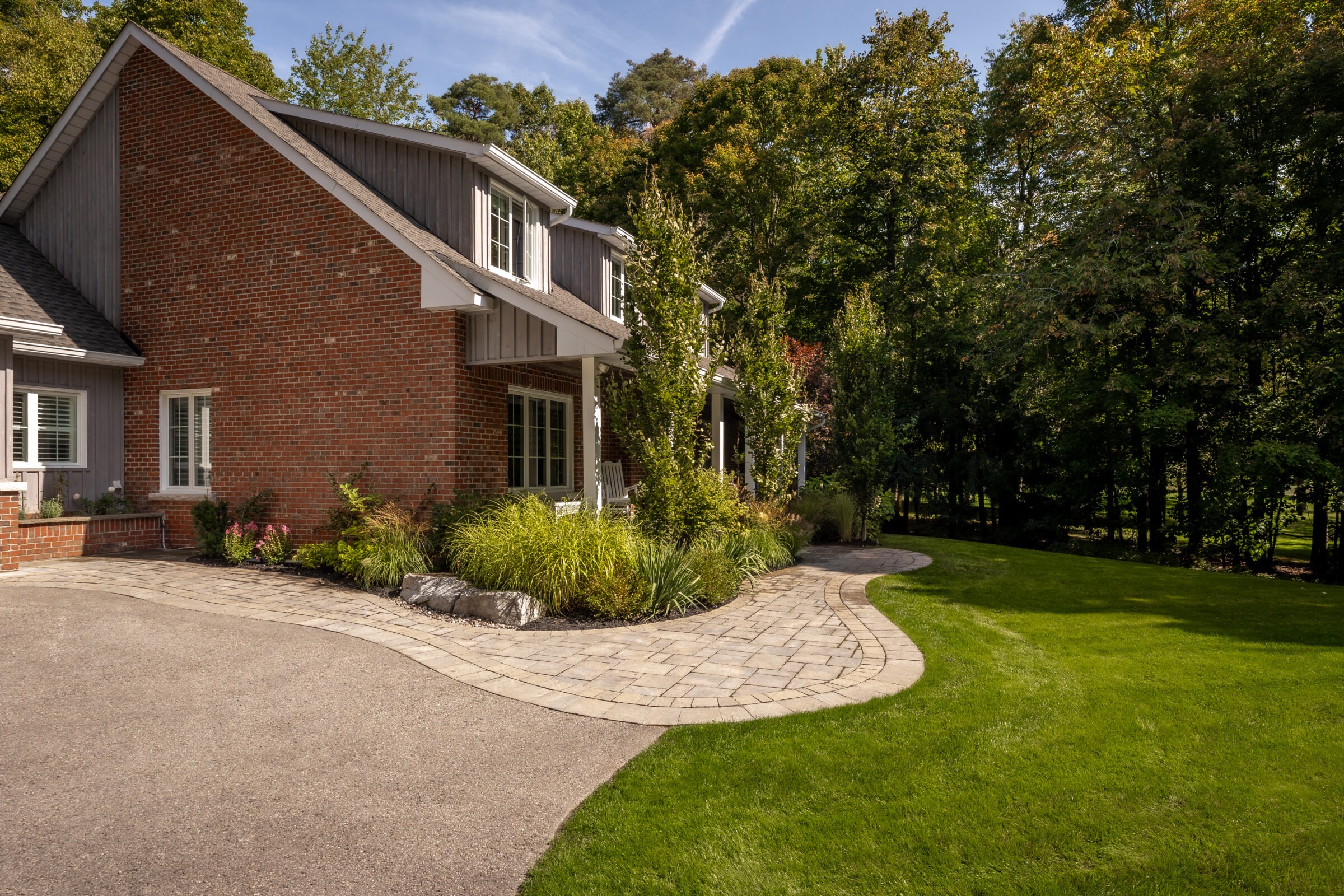 Brick house with manicured lawn and curved stone pathway, surrounded by lush greenery. No visible landmarks or historical buildings are present.