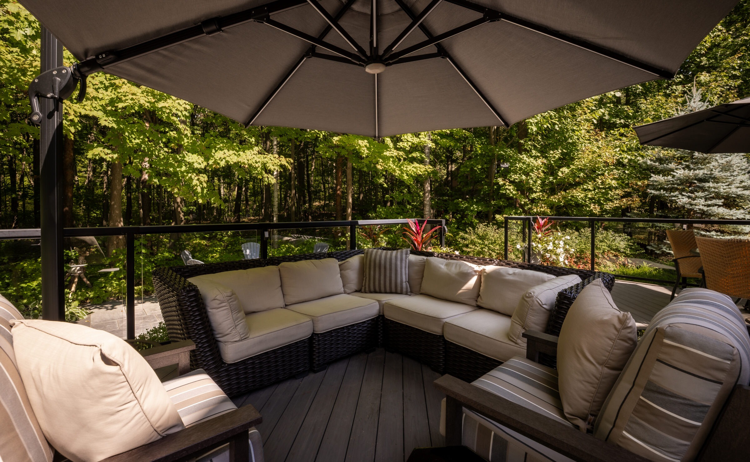 Outdoor patio area with wicker seating, cushions, and umbrellas. Surrounded by lush green forest, creating a serene, relaxing atmosphere for gatherings and leisure.